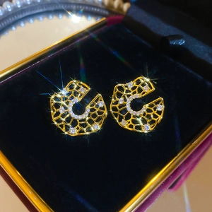 Macro shot of gold honeycomb cutout earrings with white zircons in a velvet gift box