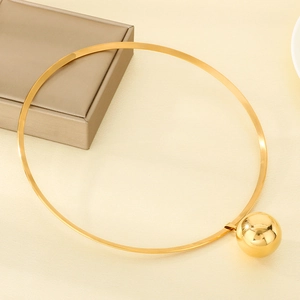 Polished gold torque necklace featuring a large hollow spherical pendant on a jewelry box
