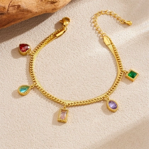 Detailed macro view of gold-plated bracelet featuring colorful gemstone charms on sand
