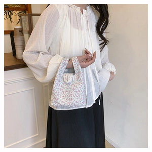 Close-up of floral print nylon handbag held by model in a soft minimalist cafe setting
