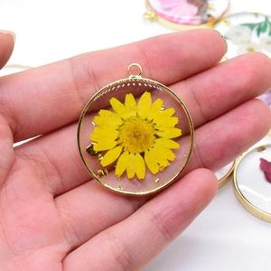 Close-up of handmade daisy flower resin pendant with gold foil and copper frame