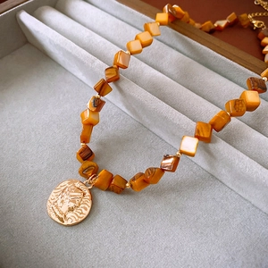 Close-up of vintage beaded necklace with square tiger eye stones and gold coin pendant
