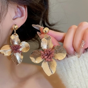 Detailed close-up of golden metal flower earrings with textured petals and brown centers