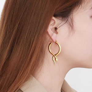 Polished gold snake-shaped crossover hoop earrings worn by a model in a luxury style