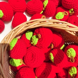Close-up of hand-knitted red apple charms made of wool yarn displayed in a wicker basket