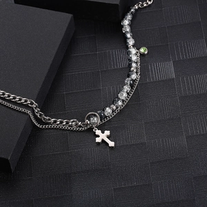 Detail of a double-layer chain bracelet featuring a silver cross and green pendant