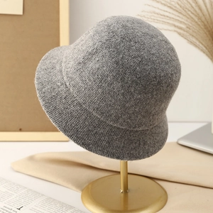 Close-up of a warm gray knitted bucket hat for women displayed on a golden metal stand