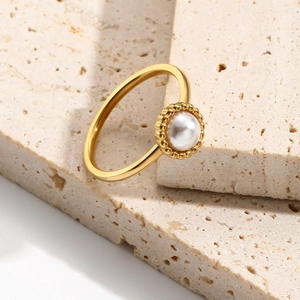 Elegant gold plated stainless steel ring with a single white pearl and textured stone decor