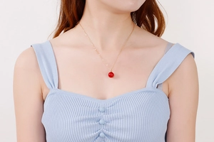 Gros plan d'un collier chaîne en or minimaliste avec un pendentif perle rouge vif