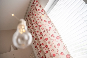 Detail of red candy pattern curtains with decorative tassels on window with blinds