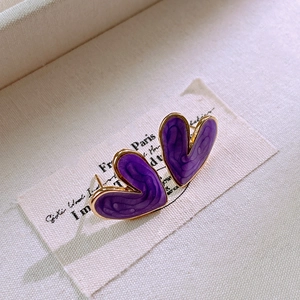 Detail of purple enamel heart earrings with gold trim on white textured fabric
