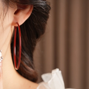 Close-up of a large red hoop earring in vintage style worn by a model in soft lighting