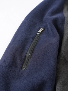 Detail of metal zipper pocket on navy and grey fleece jacket showing fabric texture