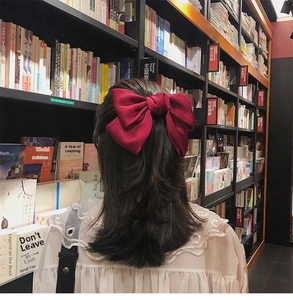 Detail view of a large red satin bow hair clip worn by a woman in a lifestyle setting