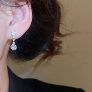 Close-up of elegant gold drop earrings featuring sparkling round zircons worn on model