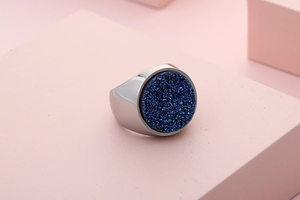 Close-up of a silver stainless steel ring with a dark blue druzy stone on a pink surface