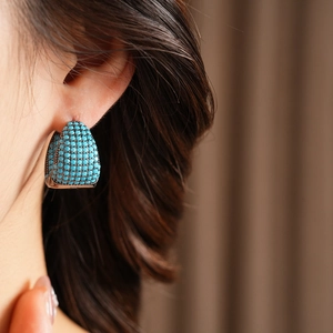 Detail of C-shaped earrings with turquoise stones worn on ear against a warm backdrop