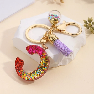 Detail of resin letter C keychain with red glitter gradient, purple tassel and gold ring
