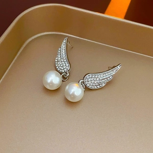 Detailed close-up of wing-shaped rhinestone earrings with white pearls on a gold tray
