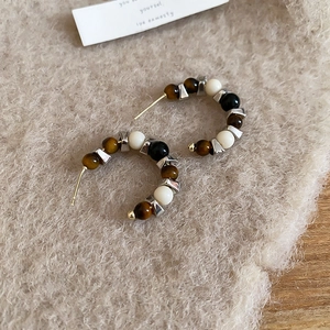 Macro detail of C-shaped hoop earrings with tiger eye beads on soft wool texture