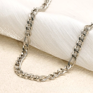 Detailed macro view of silver Figaro chain link over silk fabric background