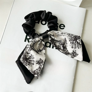 Detailed view of black satin scrunchie with long landscape print ribbons on a magazine