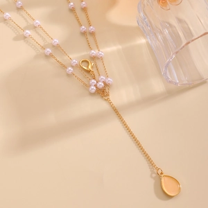 Detailed view of a gold-tone Y-necklace with purple pearls and teardrop pendant