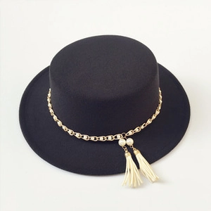 Détail d'un chapeau plat noir avec chaîne dorée, perles blanches et pompons beige