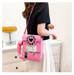 Side view of pink retro telephone shaped crossbody bag worn by a model in interior setting