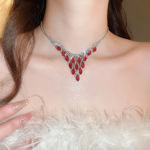 Close-up of model wearing V-shaped silver necklace with red teardrop gems and rhinestones