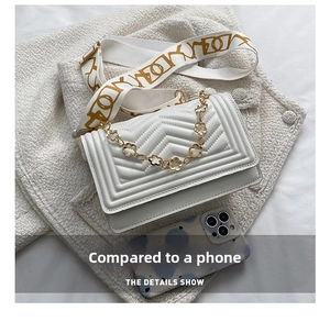 Quilted white crossbody bag with gold floral chain shown next to a smartphone for scale
