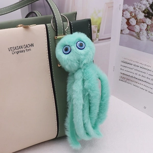 Close-up of a teal plush octopus keychain attached to a stylish beige handbag with green trim