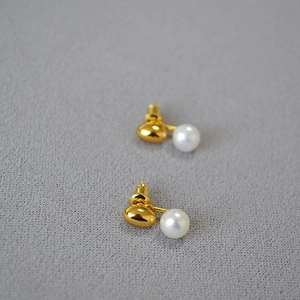 Elegant gold bean and freshwater pearl stud earrings on textured grey fabric background