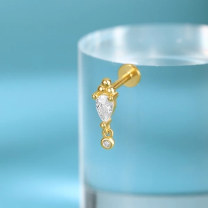 Close-up of golden cartilage piercing with teardrop and round cubic zirconia studs