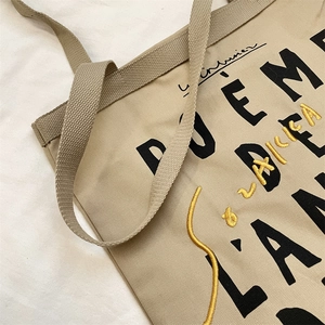 Detail of beige canvas tote bag with black lettering and yellow embroidery texture