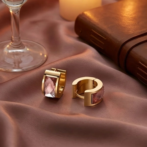 Detail of gold-plated earrings with rectangular pink faceted gemstones on satin