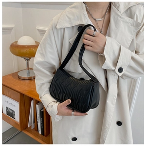Detail of a black pleated leather mini handbag held by a model in a stylish beige trench coat