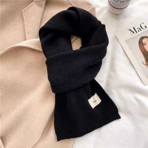 Close-up of black knitted scarf with 'emo' woven label on beige winter coat background