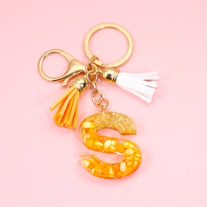 Detailed macro view of an orange resin letter S keychain with gold foil and tassel detail