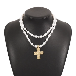 Detailed view of a double-layered pearl necklace with a textured golden cross pendant