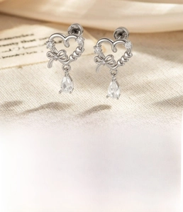 Detail of silver heart stud earrings with bow design and clear teardrop pendant drops