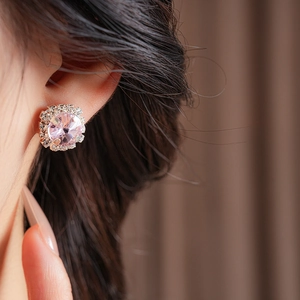 Close-up of elegant rose gold stud earrings with round pink crystal and diamond halo
