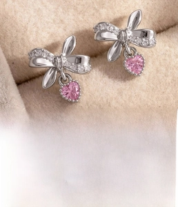 Close-up of bow earrings with pink heart crystals and clear zircons in silver finish