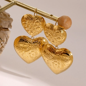 Golden double layered heart earrings with vintage floral relief patterns on a stone stand