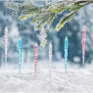 Clear acrylic Christmas icicle ornaments hanging on snowy pine branches in winter forest