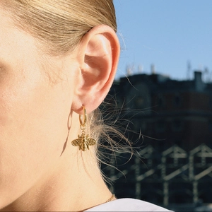 Close-up of golden bee stud earring with blue turquoise stone worn by model