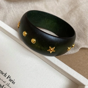 Détail du large bracelet jonc vert foncé avec rivets dorés sur texture en lin