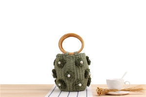 Detailed texture of green woven bucket bag featuring pearl-centered flowers and wooden handles