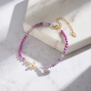 Detail of beaded bracelet featuring purple mica facets and a white pearl cross charm