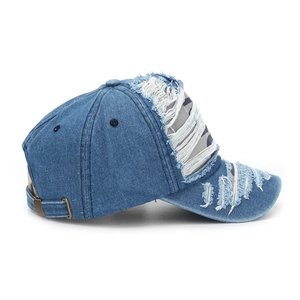 Detailed view of distressed dark blue denim baseball cap with frayed holes and vintage texture